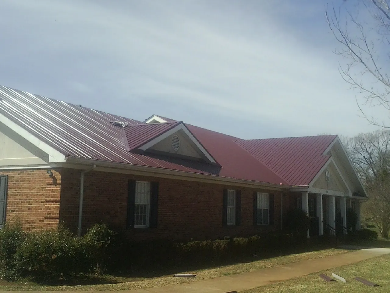 Red metal roof with gabled entries on a long brick building, from a Hail Damage Roof Repair job in Thorsby