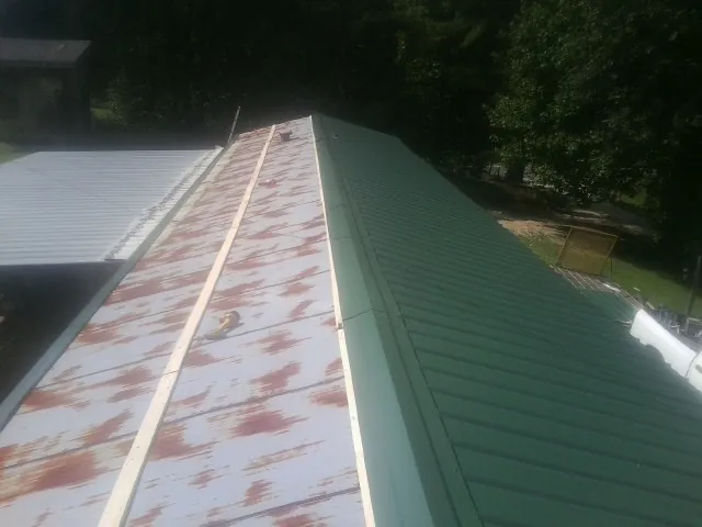 Old rusted panels beside newly installed green metal roofing — Wind Damage Roof Repair by Roofing Brothers in Thorsby