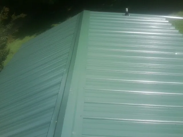 New green metal panels meeting at the ridge of a roof — Flat Roof Repair work by our crew in Thorsby