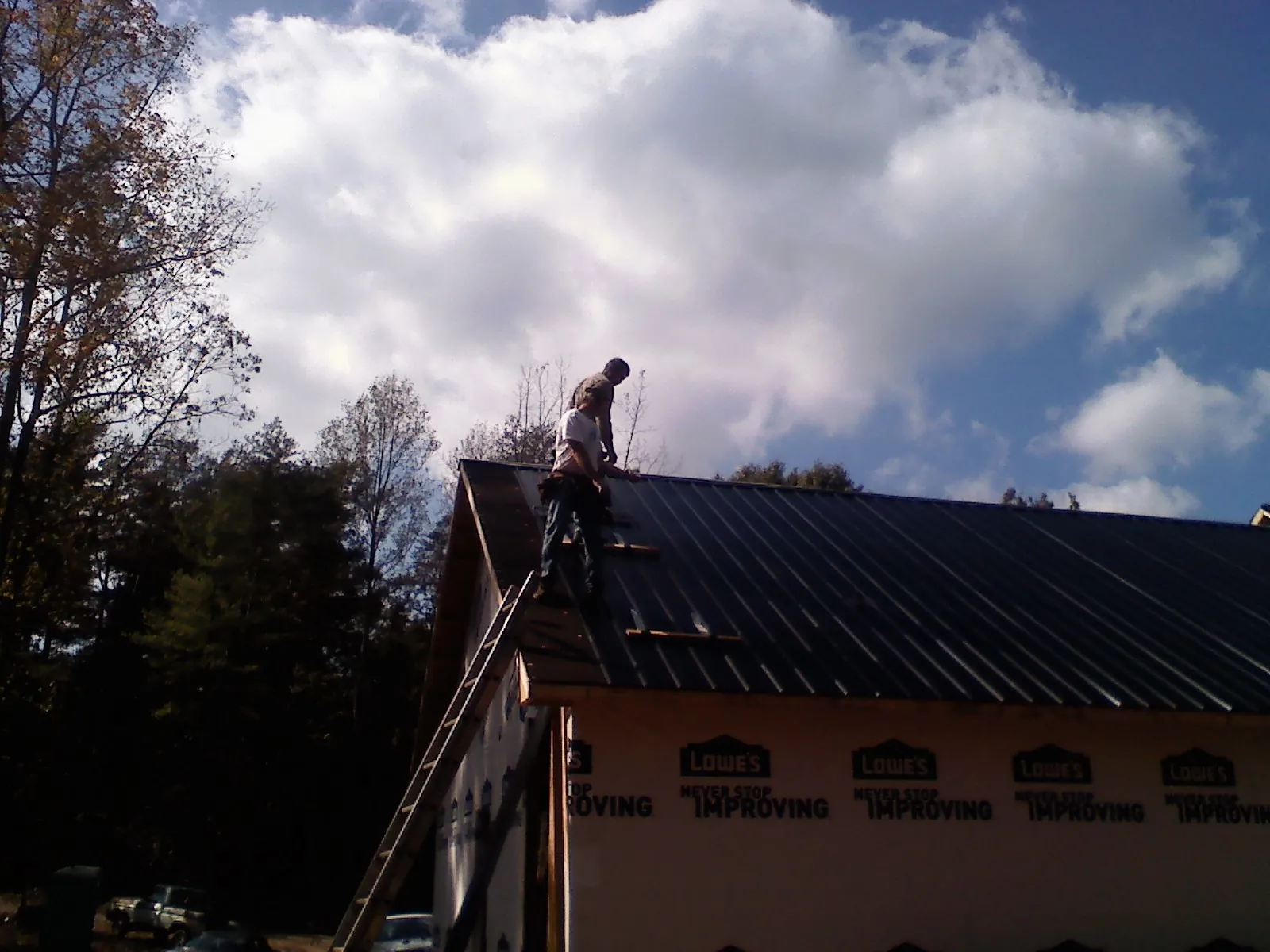 Roofer fastening dark metal panels high against a cloudy sky, from a Roof Inspection job in Thorsby