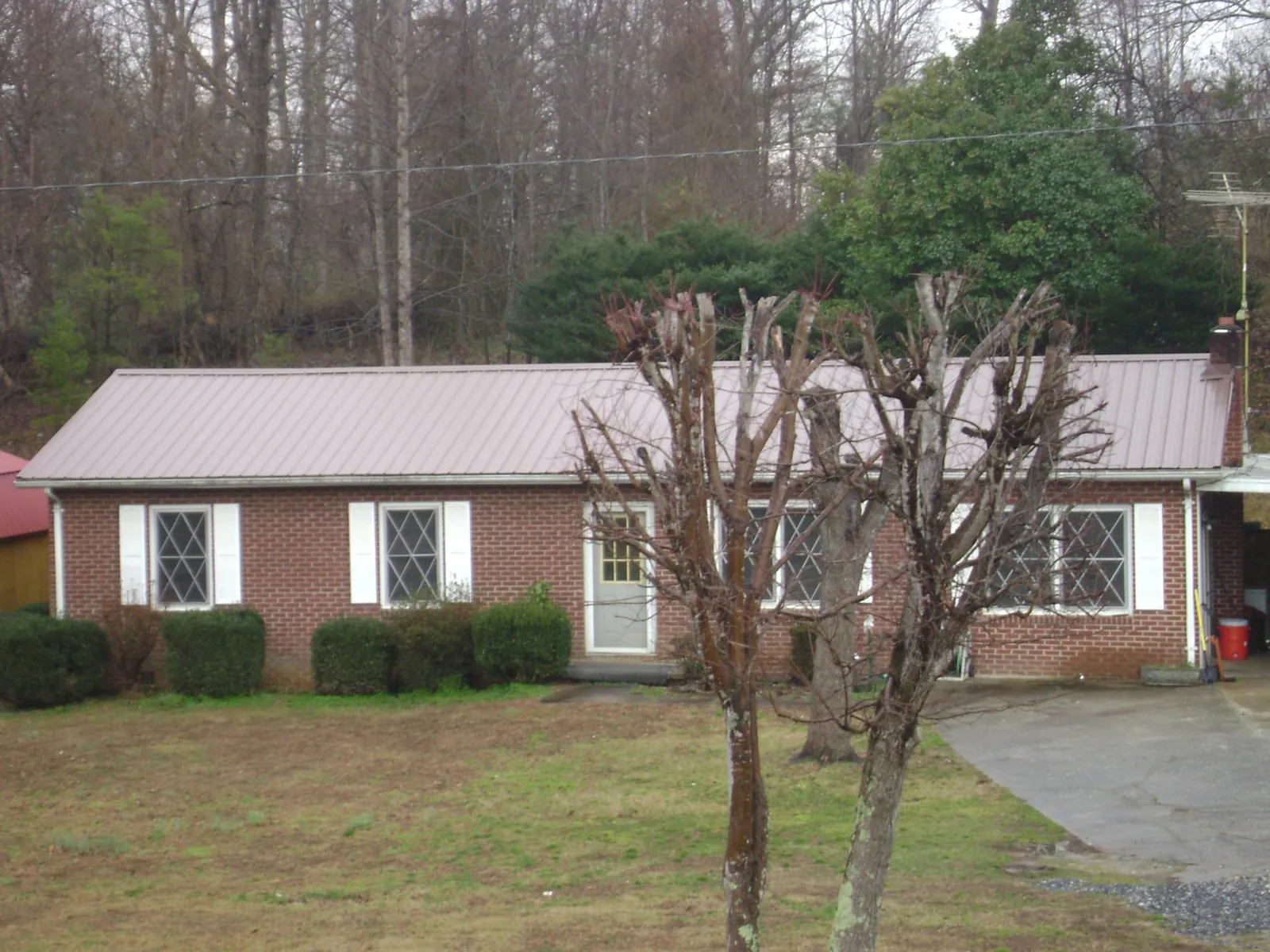 Mauve metal roof on a brick ranch home behind bare trees in Thorsby