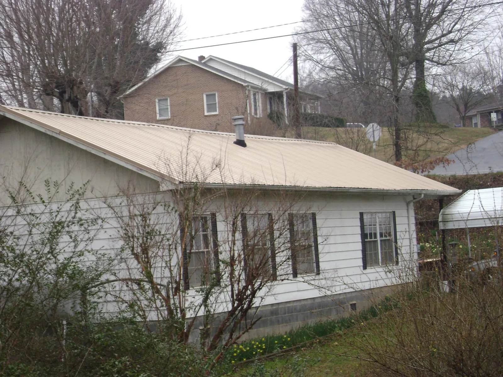 Tan metal roof on a white sided house set into a hillside — Commercial Roofing by Roofing Brothers in Thorsby